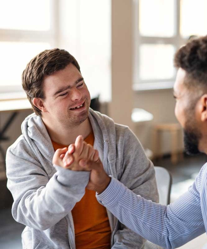 An NDIS participant and his support worker laughing and clasping hands