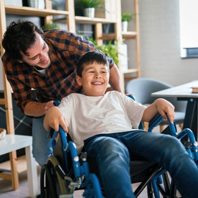 A support worker sharing a joyful moment with a young participant in his wheelchair