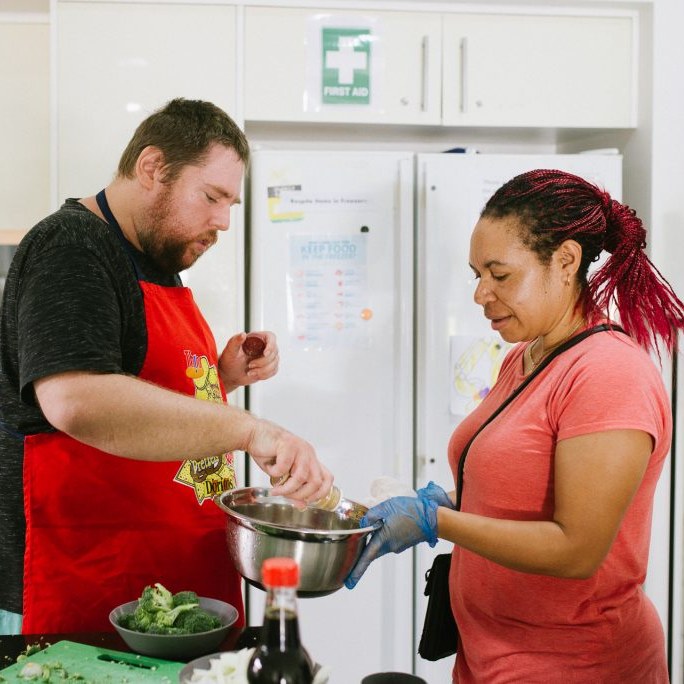 A participant and support worker cooking a meal together at home