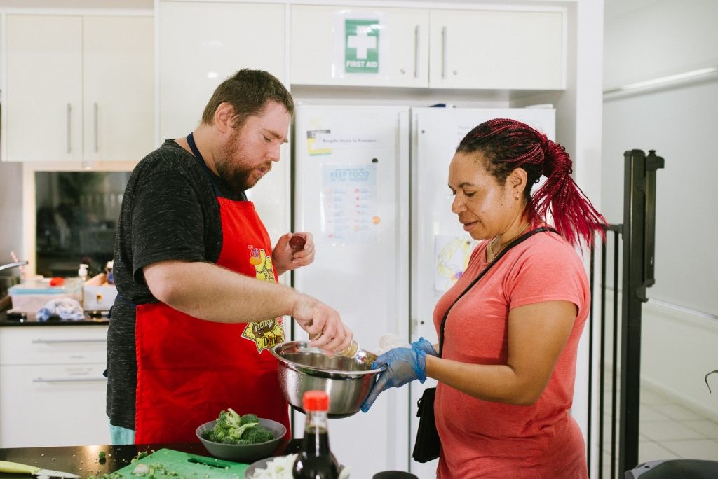 A participant and support worker cooking a meal together